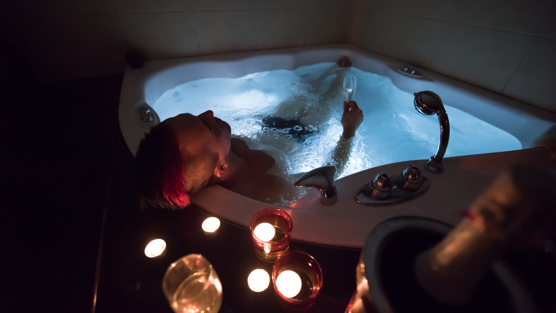 Person relaxing in a jetted bathtub at night surrounded by candles and soft ambient lighting